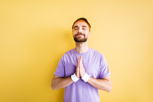 cheerful bearded sportsman with praying hands on yellow - Photo, Image
