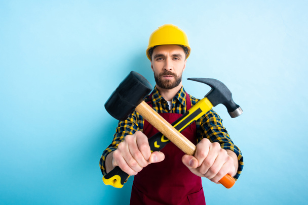 enfoque selectivo del trabajador sosteniendo martillos en azul
  - Foto, imagen