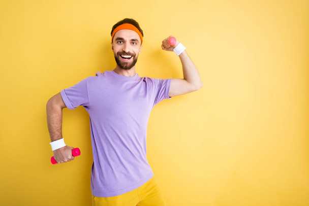 cheerful bearded sportsman holding small dumbbells while working out on yellow - Fotografie, Obrázek