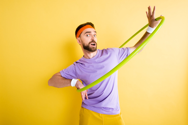 confused sportsman exercising with hula hoop on yellow - Photo, image