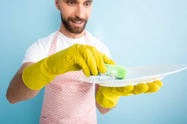 青に隔離されたスポンジで幸せな髭の男の洗濯板の選択的な焦点  - 写真・画像