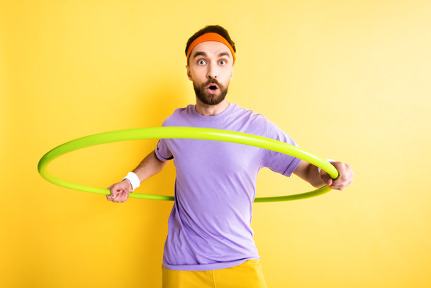 zaskoczony sportowiec ćwiczenia z hula hoop izolowane na żółto - Zdjęcie, obraz
