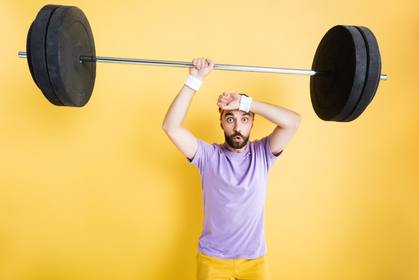 tired sportsman holding heavy barbell on yellow - Foto, Imagen