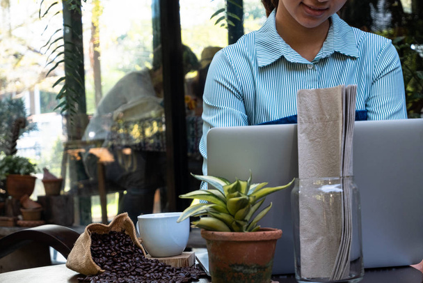 Μια γυναίκα που χρησιμοποιεί λάπτοπ για να δουλέψει και να πιει καφέ σε μια καφετέρια. - Φωτογραφία, εικόνα