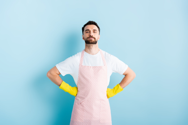 handsome bearded man in apron standing with hands on hips on blue  - Foto, imagen