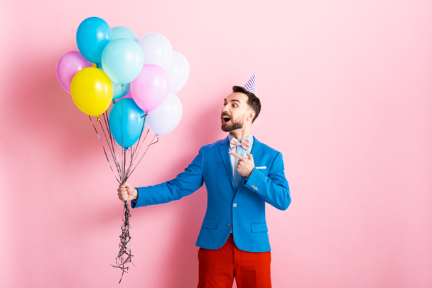 happy man in suit pointing with finger at balloons on pink  - 写真・画像