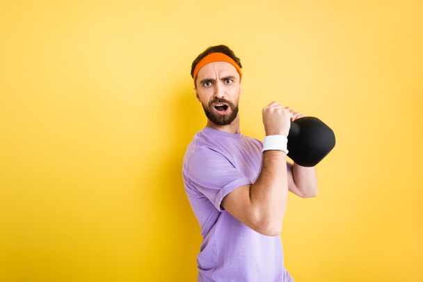 bearded man looking at camera while holding heavy dumbbell on yellow  - Φωτογραφία, εικόνα