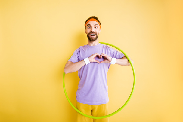 sportif heureux tenant hula hoop et montrant signe de coeur avec les mains sur jaune
 - Photo, image