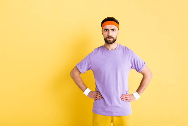 angry sportsman standing with hands on hips on yellow - Foto, imagen