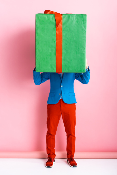 man in suit covering face while holding huge present on pink  - Foto, Bild