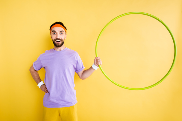 sportif gai debout avec la main sur la hanche et tenant hula hoop isolé sur jaune
 - Photo, image