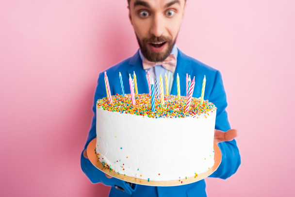 selektive Fokuskerzen auf leckerer Geburtstagstorte in den Händen eines Mannes im Anzug auf rosa  - Foto, Bild