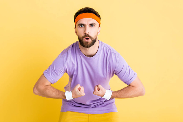 bearded sportsman in headband showing muscles isolated on yellow - Foto, imagen