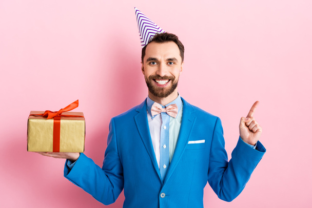 happy businessman in suit holding present and pointing with finger on pink  - Photo, Image
