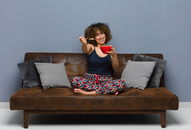 young pretty woman at home sitting on a sofa and having a breakfast - Photo, Image