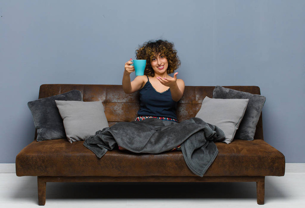 young pretty woman having a coffee mug sitting on a sofa - Foto, immagini