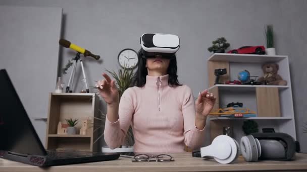 Beautiful concentrated modern woman using virtual reality headset touching something in air at home - Filmati, video