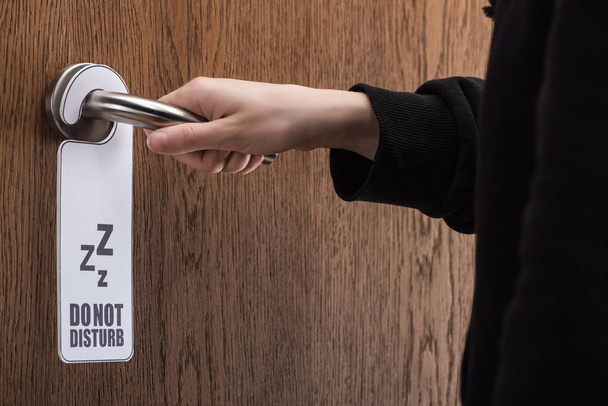 partial view of woman holding door handle with do no disturb sign  - Photo, Image