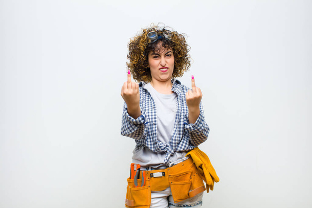 young housekeeper woman feeling provocative, aggressive and obscene, flipping the middle finger, with a rebellious attitude against white wall - Foto, afbeelding