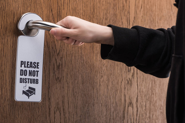 cropped view of woman holding door handle with please do no disturb sign  - Photo, Image