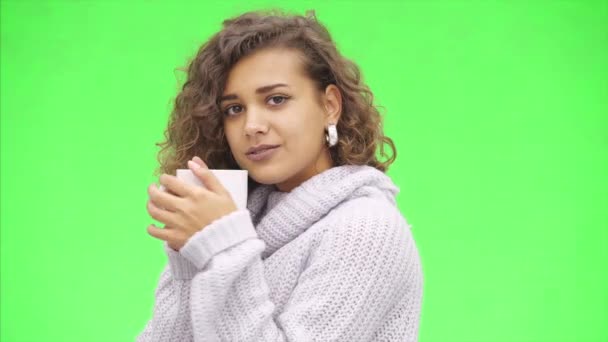 Attractive afro-american girl is holding a white mug widely. She is warming up, wearing white sweater. Close up. Copy space. - Séquence, vidéo