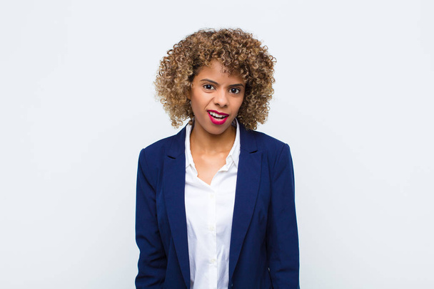 junge afrikanisch-amerikanische Frau fühlt sich verwirrt und verwirrt, mit einem stummen, fassungslosen Gesichtsausdruck, der auf etwas Unerwartetes gegen flache Wand blickt - Foto, Bild
