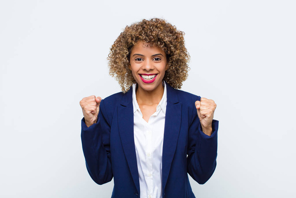 young woman african american feeling happy, positive and successful, celebrating victory, achievements or good luck against flat wall - Fotoğraf, Görsel