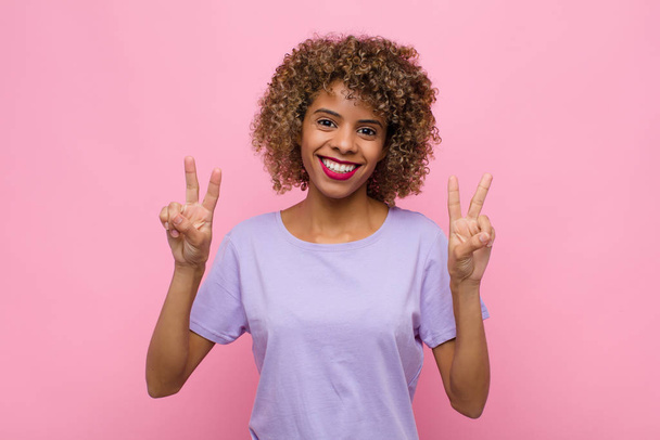 joven mujer afroamericana sonriendo y luciendo feliz, amistosa y satisfecha, haciendo un gesto de victoria o paz con ambas manos contra la pared rosa
 - Foto, imagen