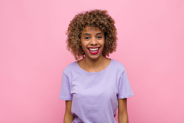 young african american woman with a big, friendly, carefree smile, looking positive, relaxed and happy, chilling against pink wall - Фото, зображення