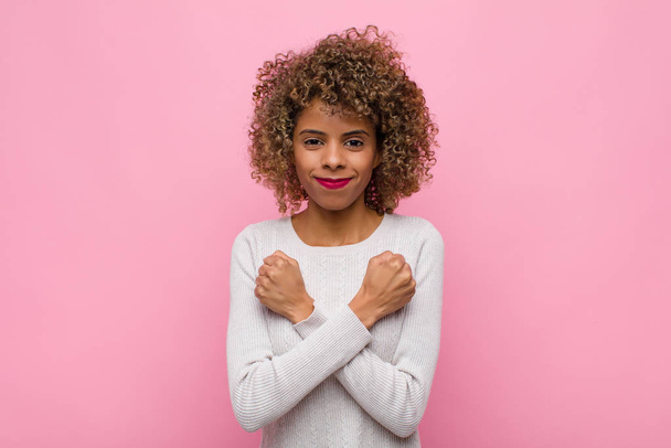 young african american woman smiling cheerfully and celebrating, with fists clenched and arms crossed, feeling happy and positive against pink wall - Foto, Bild