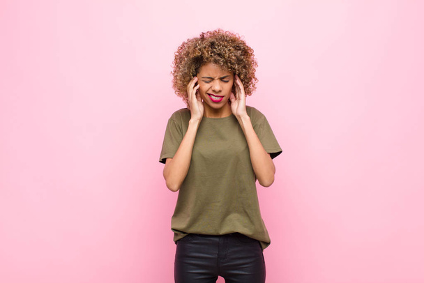 young african american woman looking angry, stressed and annoyed, covering both ears to a deafening noise, sound or loud music against pink wall - Photo, image