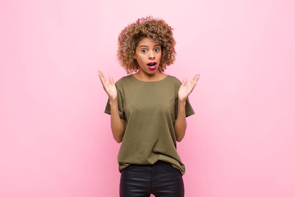 young african american woman looking shocked and astonished, with jaw dropped in surprise when realizing something unbelievable against pink wall - Foto, immagini