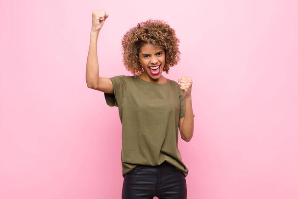young african american woman shouting triumphantly, looking like excited, happy and surprised winner, celebrating against pink wall - Foto, Imagem