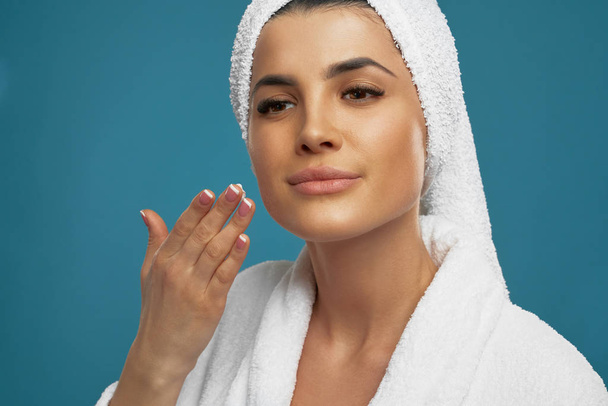 Woman in bathrobe applying cream on face. - Fotó, kép