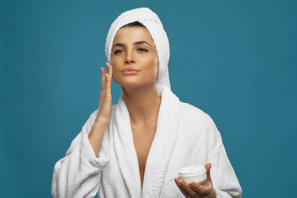 Woman in bathrobe using face cream. - Fotó, kép
