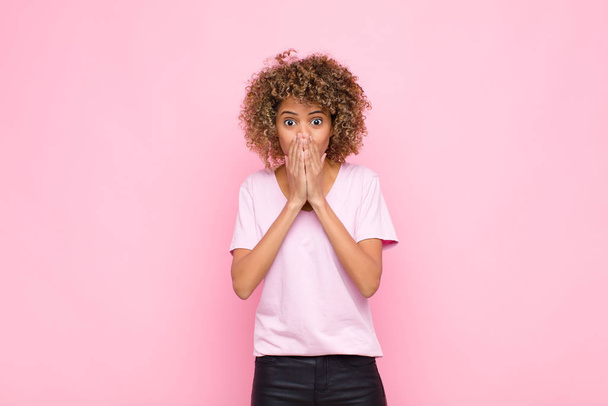 young african american woman happy and excited, surprised and amazed covering mouth with hands, giggling with a cute expression against pink wall - Fotografie, Obrázek