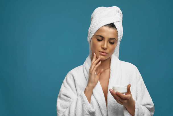 Woman in bathrobe using cream. - Фото, зображення