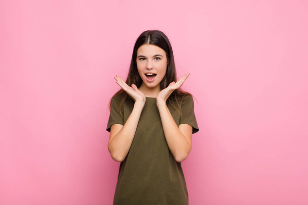 young pretty woman feeling shocked and excited, laughing, amazed and happy because of an unexpected surprise against pink wall - Fotoğraf, Görsel