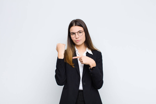 young businesswoman looking impatient and angry, pointing at watch, asking for punctuality, wants to be on time against white wall - Photo, image