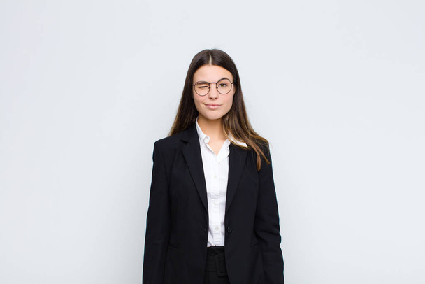 young businesswoman looking happy and friendly, smiling and winking an eye at you with a positive attitude against white wall - Fotoğraf, Görsel