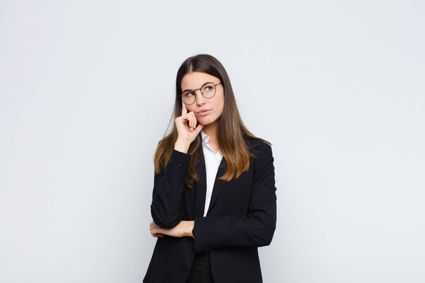 young businesswoman with a concentrated look, wondering with a doubtful expression, looking up and to the side against white wall - Fotoğraf, Görsel