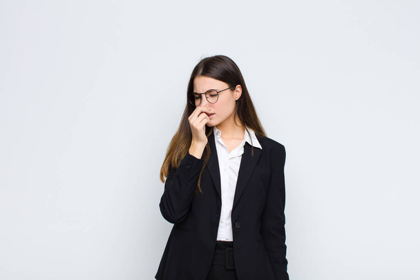 young businesswoman feeling disgusted, holding nose to avoid smelling a foul and unpleasant stench against white wall - Fotoğraf, Görsel