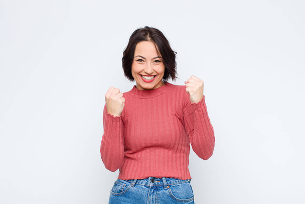 young pretty woman shouting triumphantly, laughing and feeling happy and excited while celebrating success against white wall - Fotoğraf, Görsel