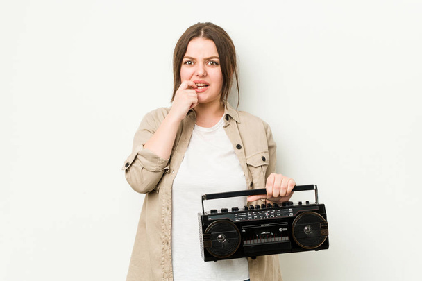 Fiatal görbe nő kezében egy retro rádió harapás körmök, ideges és nagyon ideges. - Fotó, kép