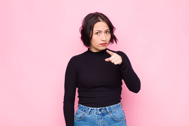 young pretty woman pointing at camera with an angry aggressive expression looking like a furious, crazy boss against pink wall - Foto, afbeelding
