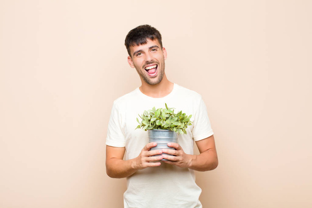 young handsome man with cheerful, carefree, rebellious attitude, joking and sticking tongue out, having fun holding a plant - Foto, Imagen