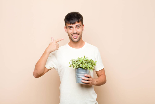young handsome man smiling confidently pointing to own broad smile, positive, relaxed, satisfied attitude holding a plant - Foto, immagini