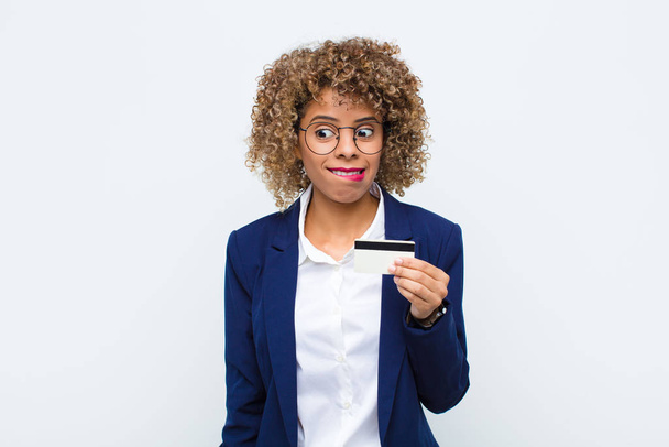 young african american woman looking puzzled and confused, biting lip with a nervous gesture, not knowing the answer to the problem with a credit card - Photo, Image