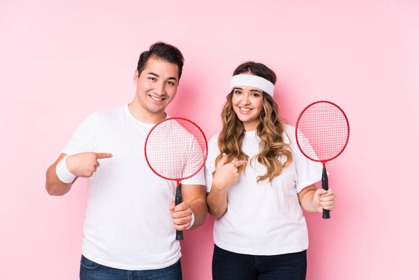 Giovane coppia che gioca badminton persona isolata che punta a mano ad uno spazio copia camicia, orgoglioso e fiducioso - Foto, immagini