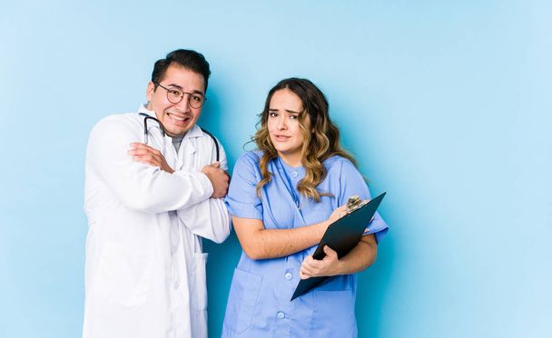 Joven pareja de médicos posando en un fondo azul aislado pasando frío debido a baja temperatura o una enfermedad
. - Foto, Imagen